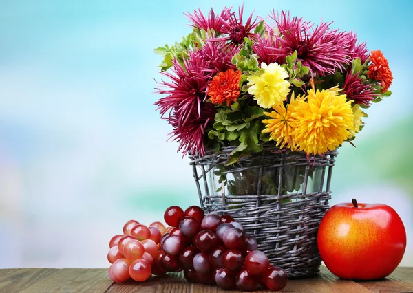 Composition with beautiful flowers in wicker vase and fruits,  on bright background — Stock Photo, Image
