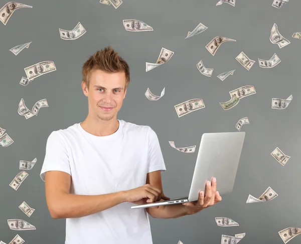 在灰色的背景上的钱雨在笔记本电脑上工作的年轻人 — 图库照片