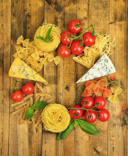Different pasta, cheese and tomatoes on wooden table close-up — Stock Photo, Image