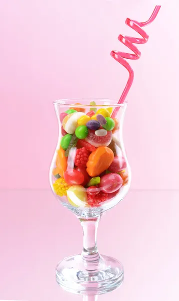 Różne kolorowe cukierki owocowe w szkle na różowym tle — Zdjęcie stockowe