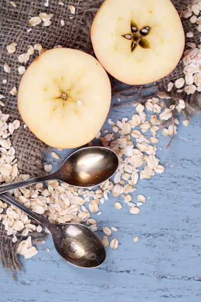 Apple with oatmeal and vintage spoons on sackcloth, on color wooden background — Stock Photo, Image