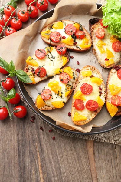 Tasty bruschetta with tomatoes on pan, on old wooden table — Stock Photo, Image