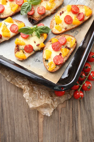 Tasty bruschetta with tomatoes on pan, on old wooden table — Stock Photo, Image