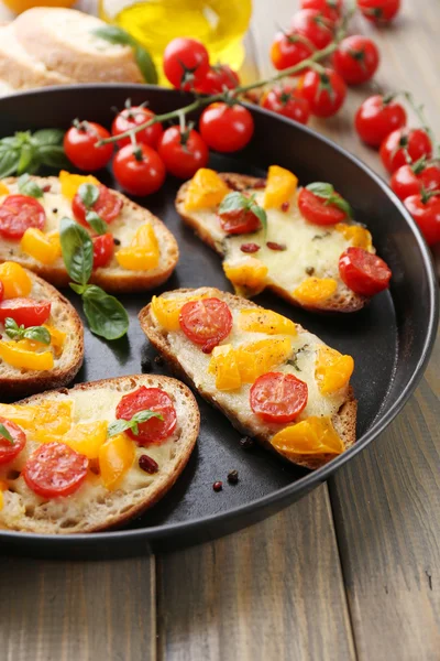 Sabroso bruschetta con tomates en la cacerola, en la mesa de madera vieja —  Fotos de Stock