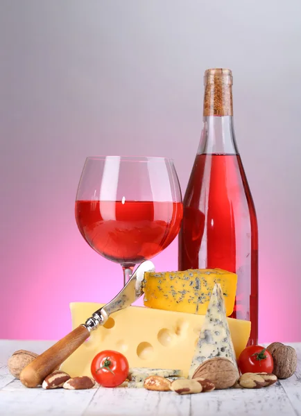 Pink wine and different kinds of cheese on colorful background — Stock Photo, Image