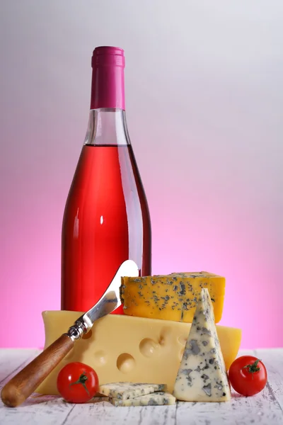 Pink wine and different kinds of cheese on colorful background — Stock Photo, Image
