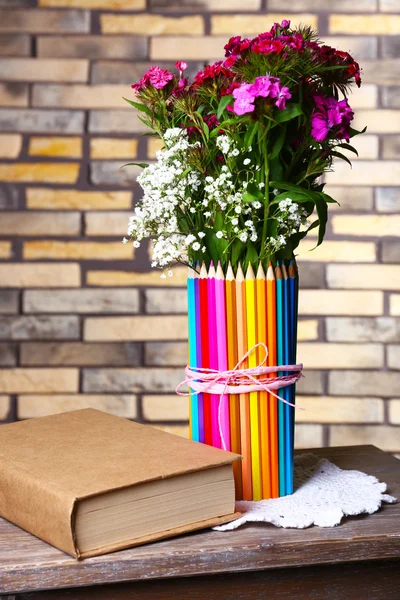 Vackra blommor i färgglada pennor vas på tegel vägg bakgrund — Stockfoto