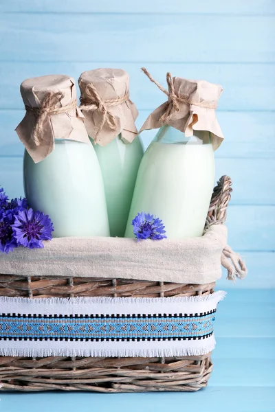 Bottles of milk and cornflowers in wicker basket on wooden background — Stock Photo, Image