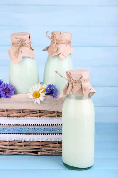 Пляшки молока та квітів у плетеному кошику на дерев'яному фоні — стокове фото
