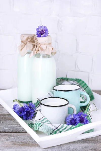 Garrafas e xícaras de leite com flores de milho em bandeja de madeira — Fotografia de Stock