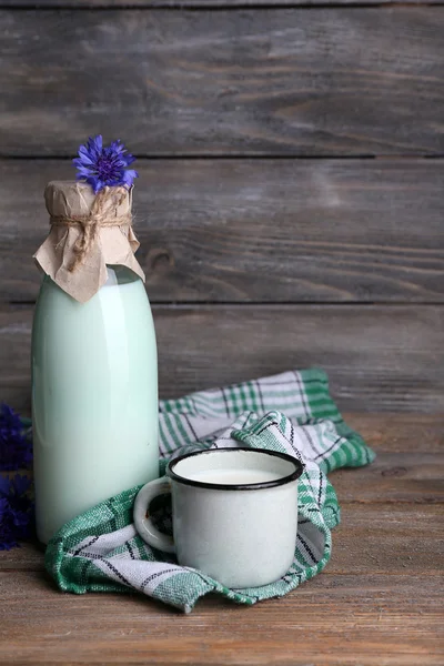 Garrafa e xícara de leite com flores de milho em fundo de madeira — Fotografia de Stock
