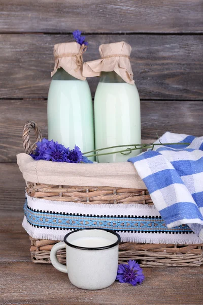 Bottles of milk and cornflowers in wicker basket on wooden background — Stock Photo, Image