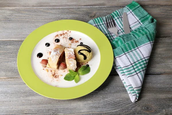 Tasty homemade apple strudel with nuts, mint leaves and ice-cream on plate, on wooden background — Stock Photo, Image