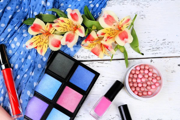 Oogschaduw, penseel, lippenstift en bloemen op een houten achtergrond kleur — Stockfoto