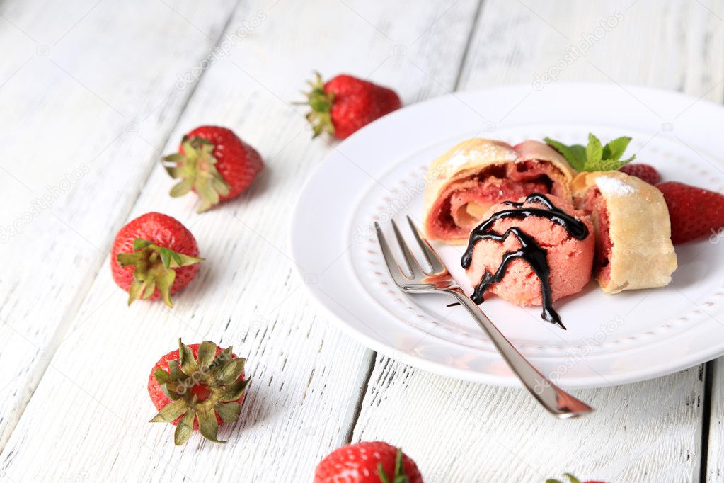 Tasty homemade strudel with ice-cream, fresh strawberry and mint leaves on plate, on wooden background