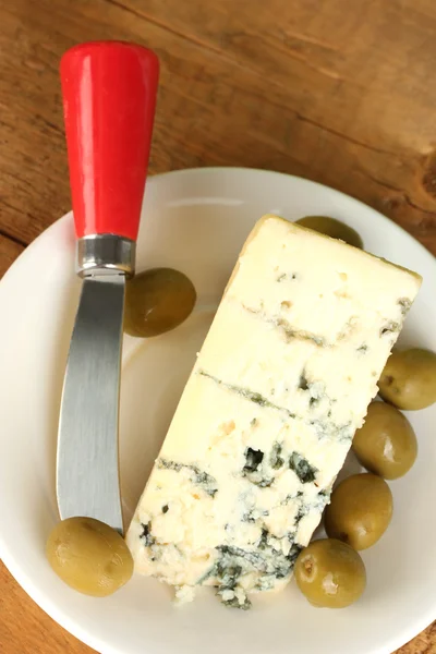 Cheese with mold and olives on the plate and knife on wooden background close-up — Stock Photo, Image