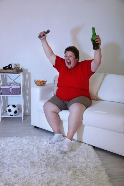 Preguiçoso excesso de peso masculino sentado no sofá e assistindo televisão — Fotografia de Stock
