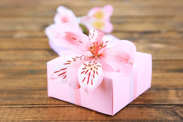 Presente rosa com arco e flor na mesa de madeira close-up — Fotografia de Stock