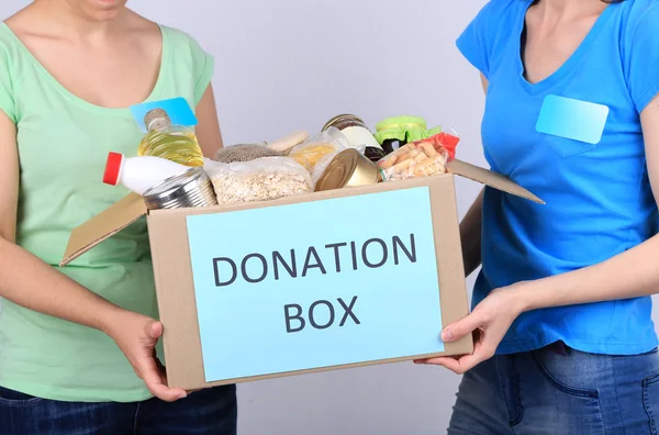 Εθελοντές με κουτί δωρεών με τρόφιμα σε γκρι φόντο — Φωτογραφία Αρχείου