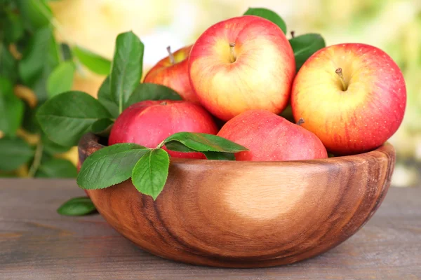 Olgun tatlı elma doğa zemin üzerine ahşap kase yaprak ile — Stok fotoğraf