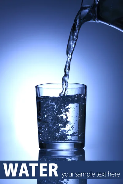 Häll vatten från kannan i glas, på Mörkblå bakgrund — Stockfoto