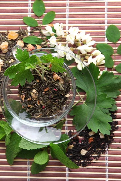 Стеклянная чашка с сухими цветами и травами ингредиенты для чая, на бамбуковом фоне мат — стоковое фото