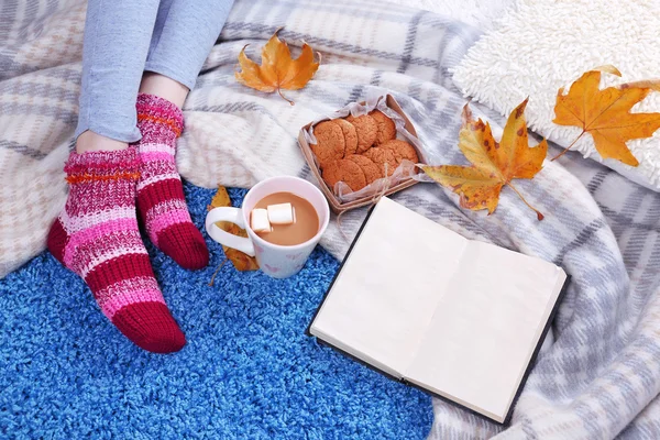 Komposition mit warmem Karo, Buch, Tasse Heißgetränk und weiblichen Beinen, auf farbigem Teppich Hintergrund — Stockfoto