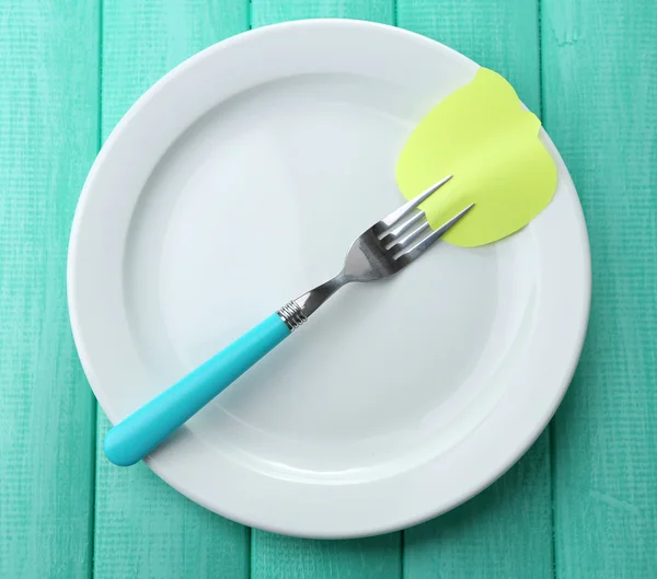 Empty note paper attached to fork, on plate, on color wooden background — Stock Photo, Image