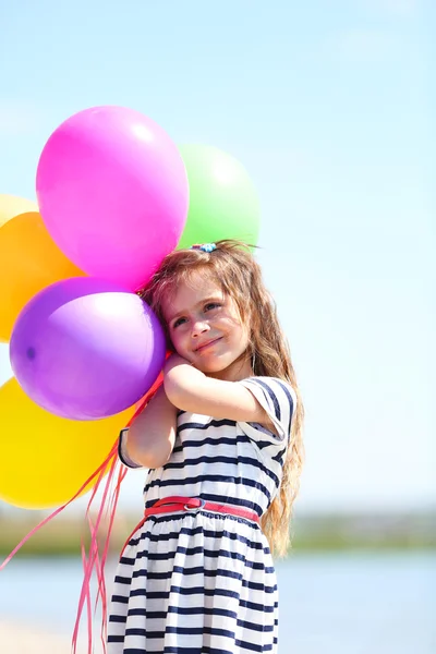 Vacker liten flicka med färgglada ballonger på stranden — Stockfoto