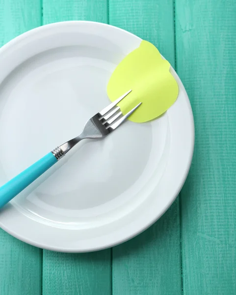 Empty note paper attached to fork, on plate, on color wooden background — Stock Photo, Image