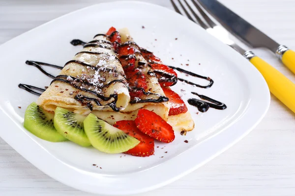 Delicious pancakes with strawberries and chocolate on plate on table — Stock Photo, Image