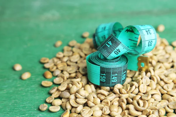 Syrové zelené kávové boby a měřicí pásky, na barevné dřevěné pozadí. Koncepce úbytku hmotnosti — Stock fotografie