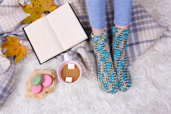 Composition avec plaid chaud, livre, tasse de boisson chaude et jambes féminines, sur fond de tapis de couleur — Photo