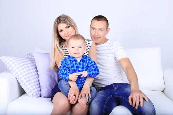 Jovem casal feliz com bebê pequeno no sofá no quarto — Fotografia de Stock