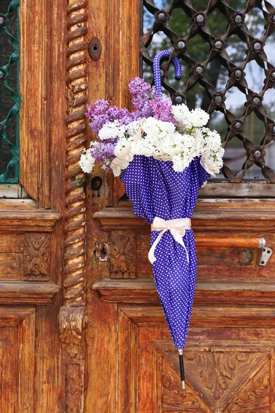 Beautiful lilac flowers in umbrella on old wooden doors — Stock Photo, Image