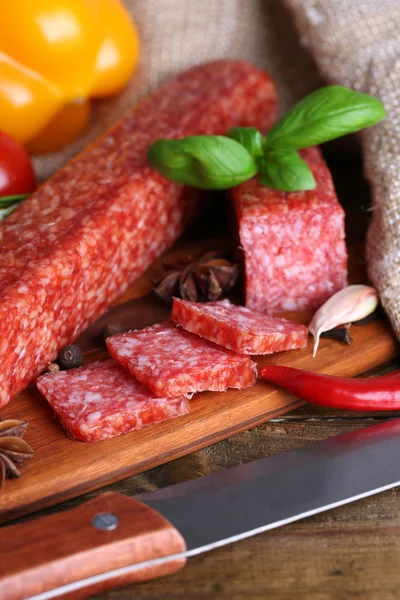 Tasty salami sausage and spices on wooden background — Stock Photo, Image