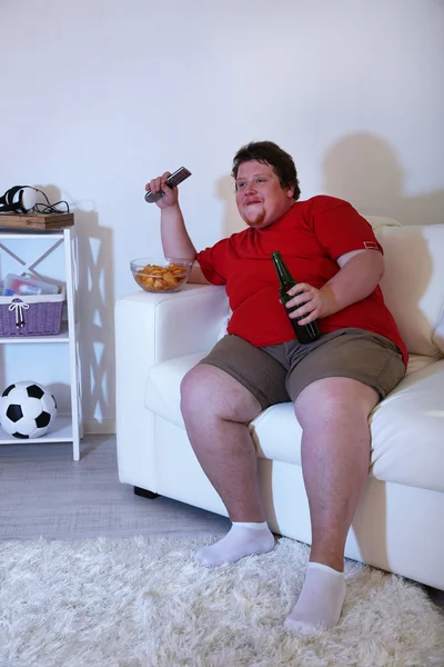 Preguiçoso excesso de peso masculino sentado no sofá e assistindo televisão — Fotografia de Stock