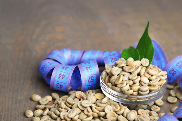 Chicchi di caffè verde grezzo in tazza di vetro e nastro di misura, su sfondo di legno a colori. Concetto di perdita di peso — Foto Stock