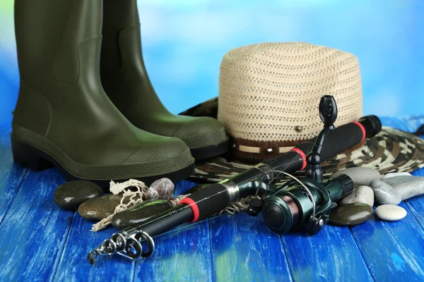 Angelrute, Gummistiefel und Hut auf Holztisch vor natürlichem Hintergrund — Stockfoto