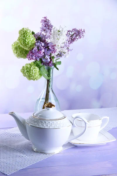 Composição com bule, caneca e belas flores de primavera em vaso, na mesa de madeira, no fundo brilhante — Fotografia de Stock