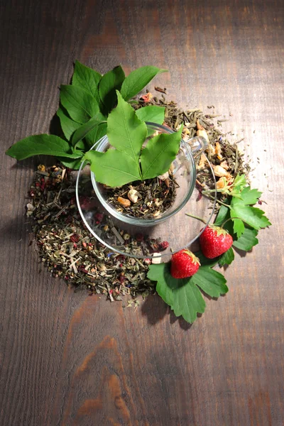 Стеклянная чашка с сухими цветами и травами, фрукты ингредиенты для чая, на цветном деревянном фоне — стоковое фото