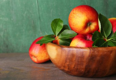 Tahta zeminde yaprakları olan olgun elmalar.