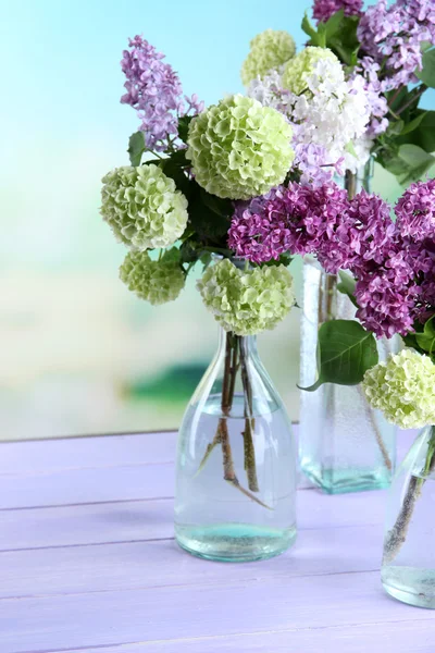 Красивые весенние цветы в стеклянных бутылках, на деревянном столе, на ярком фоне — стоковое фото