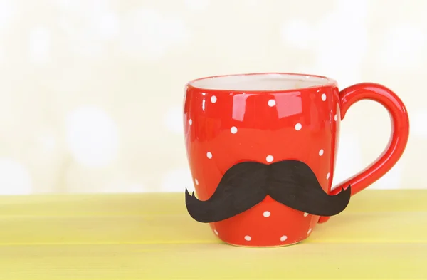 Cup with mustache on table on light background — Stock Photo, Image