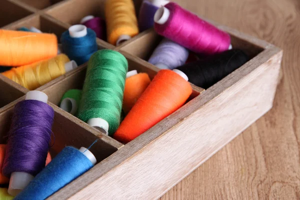 Hilo de coser multicolor en caja de madera, sobre fondo de madera, primer plano —  Fotos de Stock