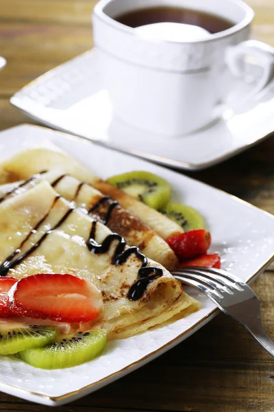 Heerlijke pannenkoeken met aardbeien en chocolade op plaat op tafel — Stockfoto