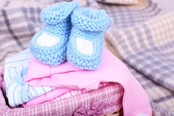 Baby clothes in basket on plaid in room — Stock Photo, Image