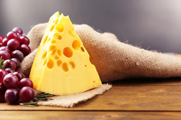 Pedaço de queijo com uva e alecrim sobre mesa de madeira, sobre fundo escuro — Fotografia de Stock
