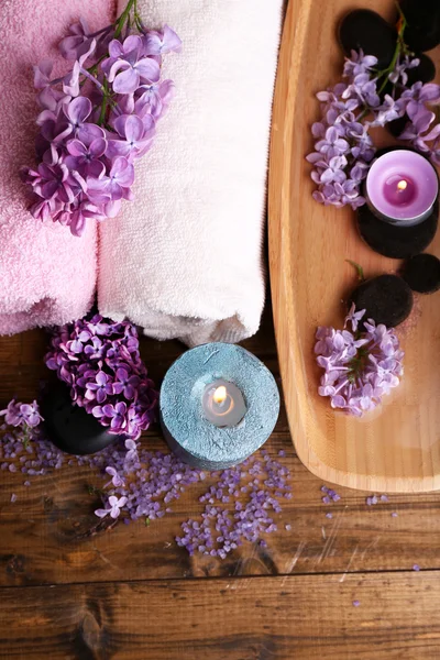 Sammansättning med spa-behandling, trä skål med vatten, handduk och lila blommor, på trä bakgrund — Stockfoto