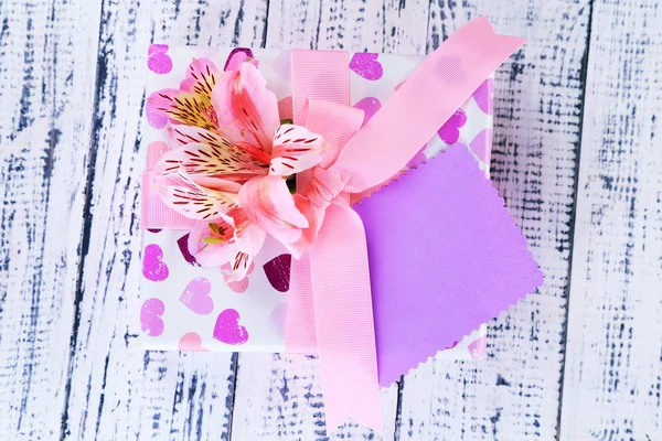 Розовый подарок с луком и цветами на деревянном столе крупным планом — стоковое фото